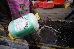 Protester pours liquid out of a drum that reads 