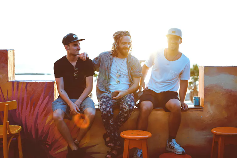 Three men sit next to each other chatting in the sunset