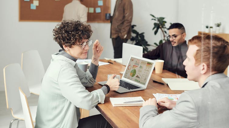 Business people sit around a table with laptops and documents open