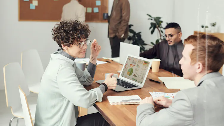 Business people sit around a table with laptops and documents open