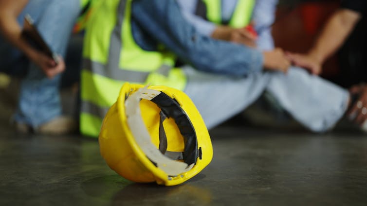 yellow hard hat on ground. people are nearby sitting on ground after an accident
