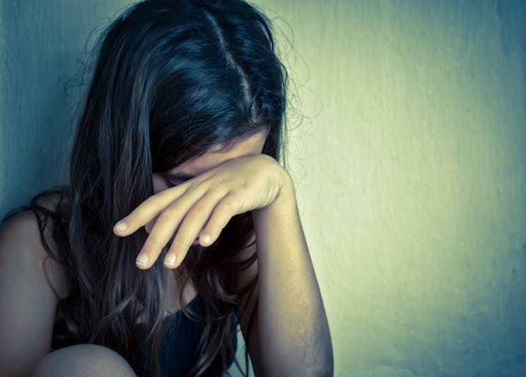 Girl or teenager leaning against wall, hand across face, looking down