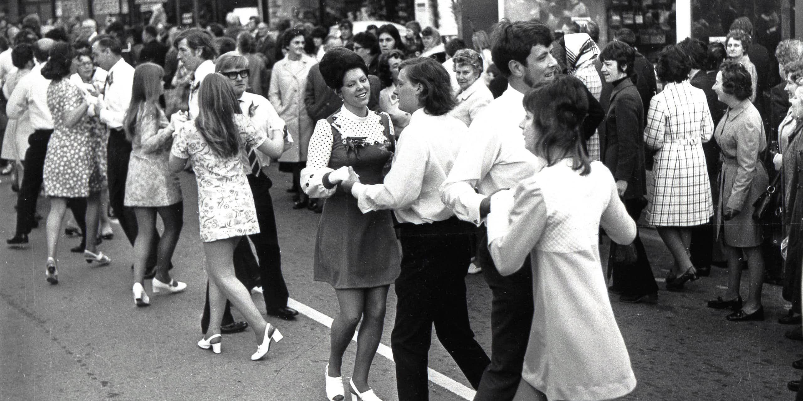 An archival black and white photograph of young people dancing in the street.