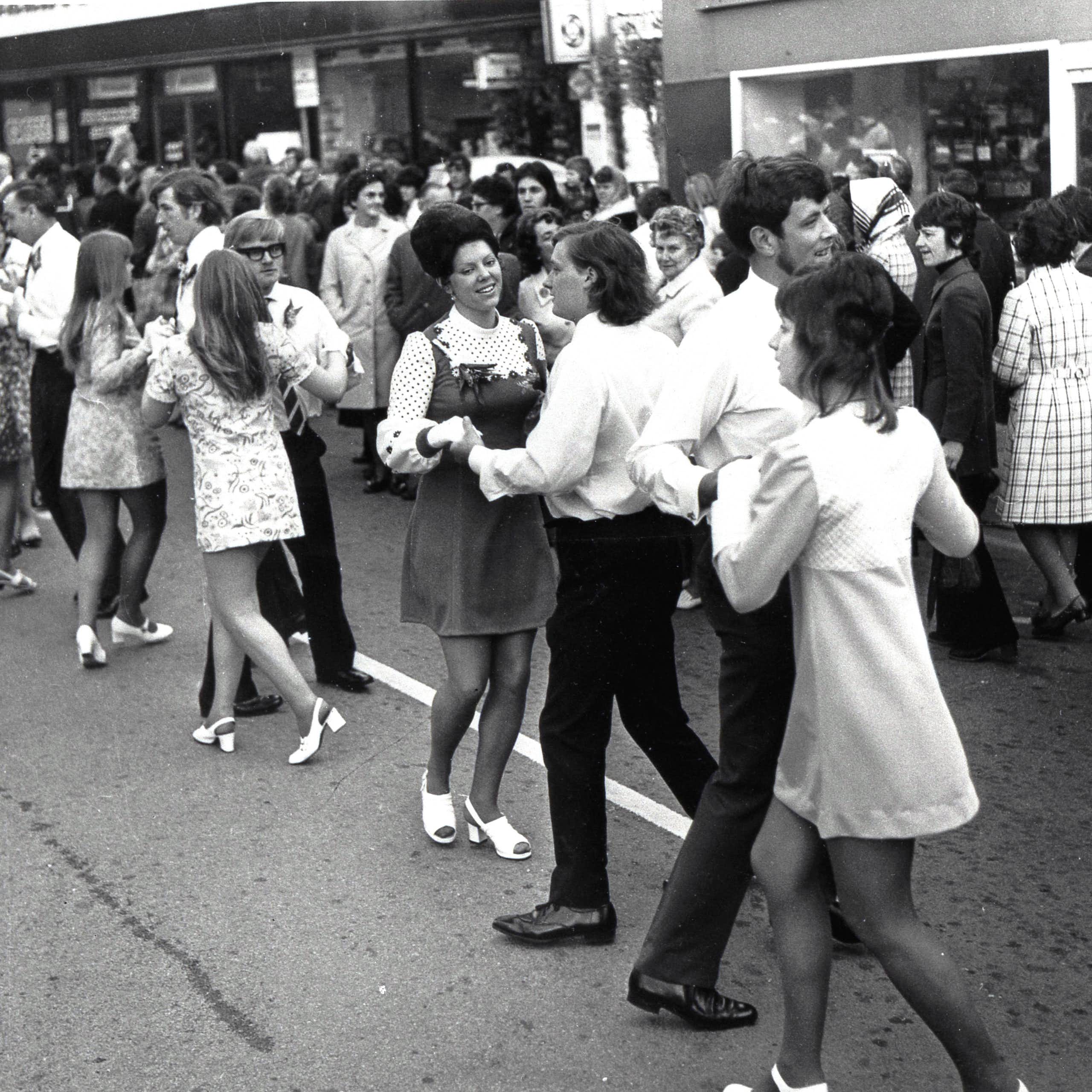 An archival black and white photograph of young people dancing in the street.