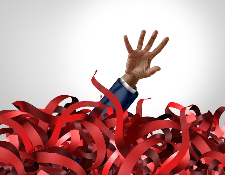 Hand emerging from swirls of red tape.