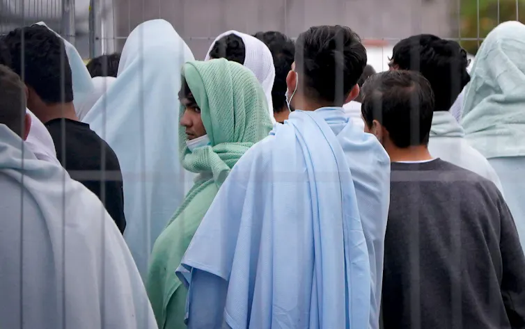 A group of young men, many wrapped in blankets, seen through a fence