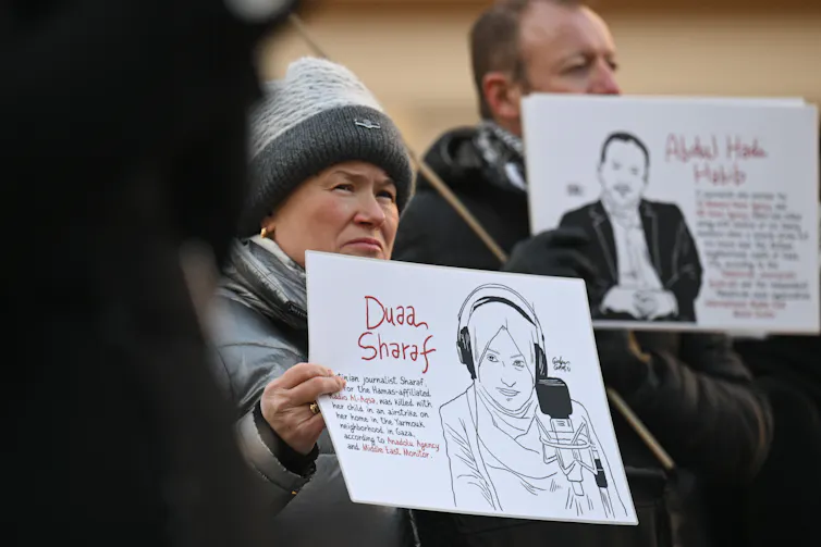 A woman and man hold posters with the names of journalists who have been killed.