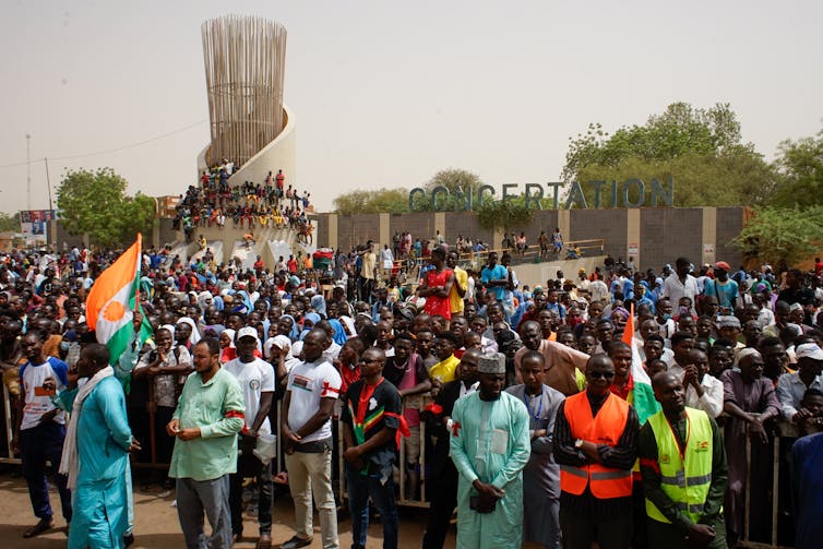 A crowd of Nigeriens with one person waving a Niger flag gathered in protest.