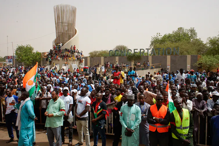 Une foule de Nigériens, dont une personne brandissant un drapeau nigérien, s'est rassemblée pour protester.