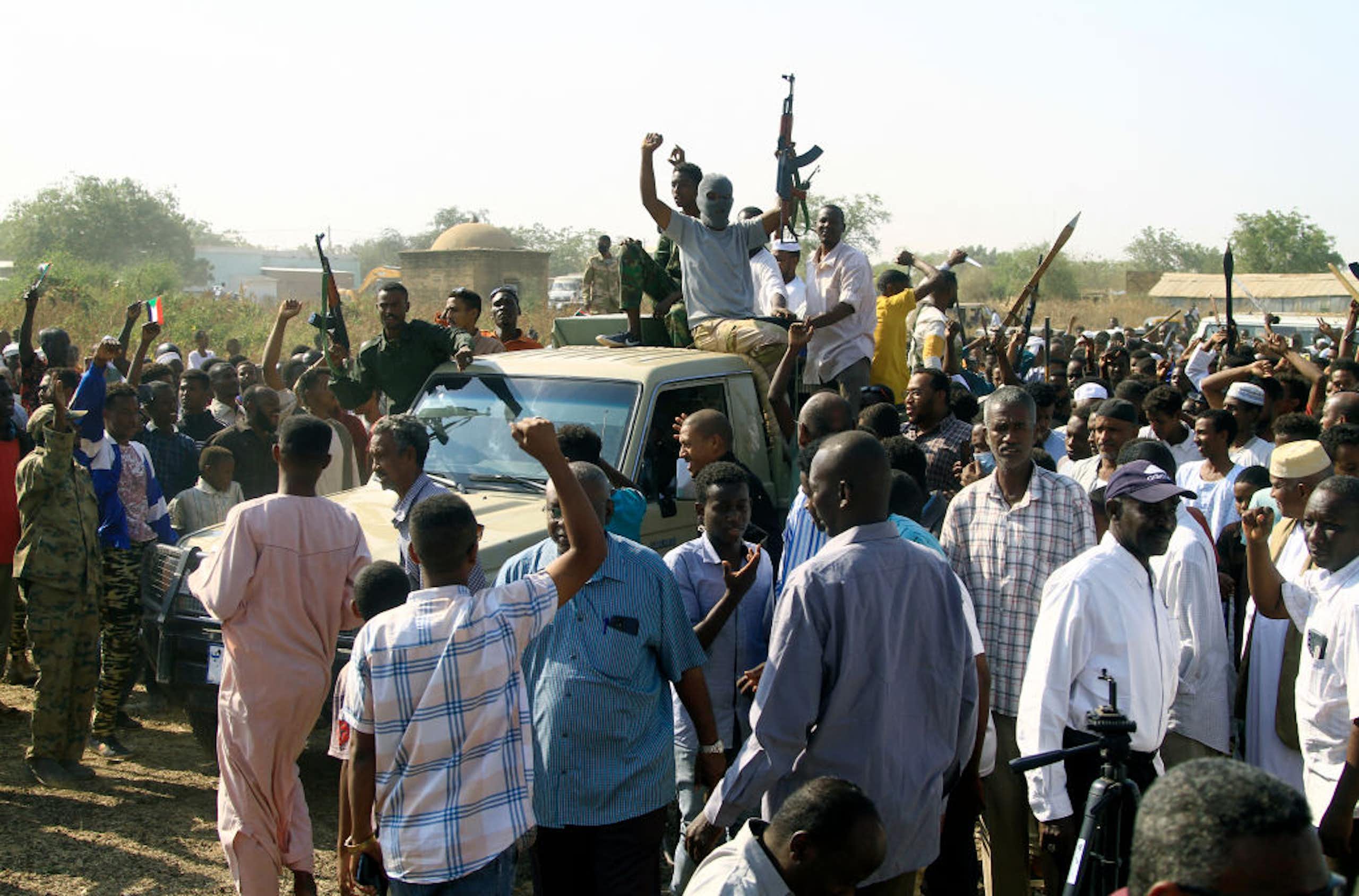 Men surrounding a pick-up track lifting guns and their arms in the air