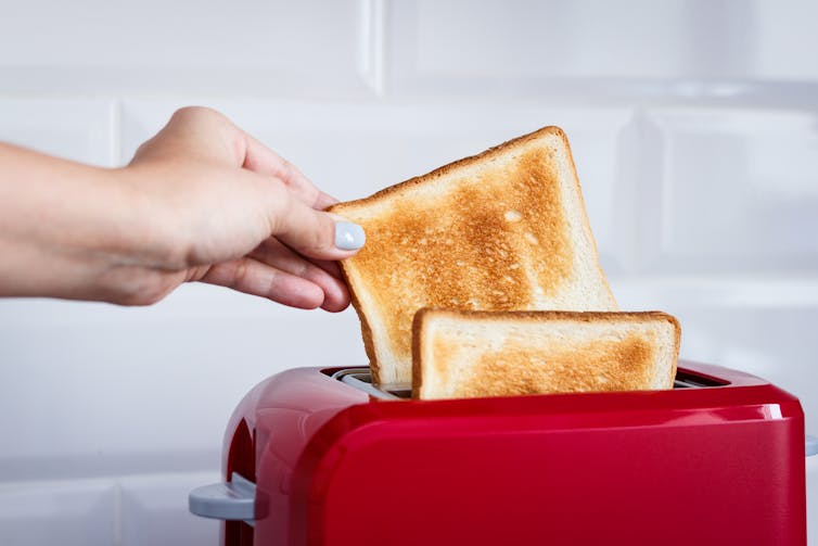 A person's hand grabs a slice of toast out of a red toaster.