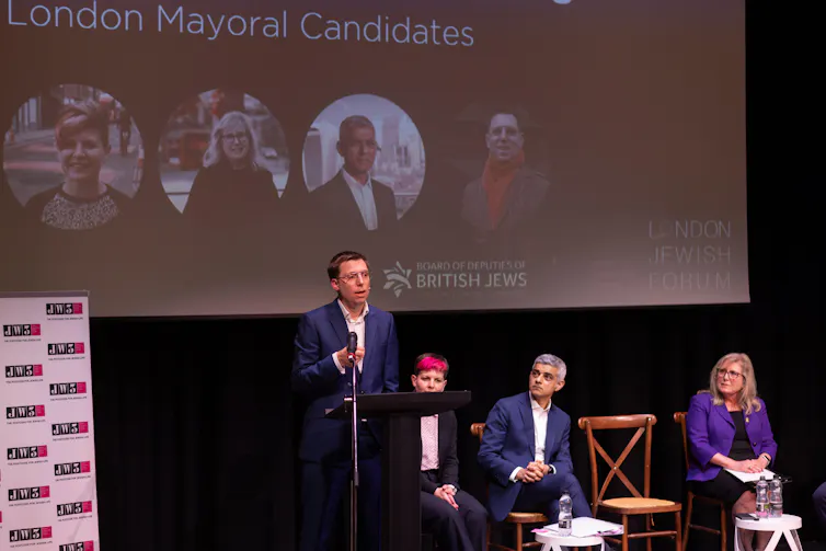 Mayoral candidates sit and stand on stage.