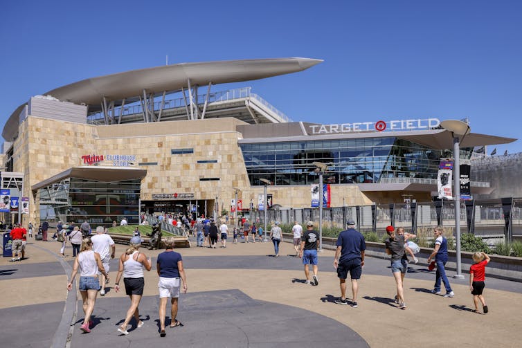People walk toward a baseball park. A sign over the entrance reads 'Target Field,' with the Target Corporation's red bullseye symbol.
