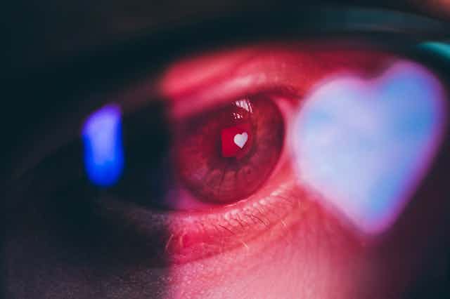 Close up of a human eye with a heart reflected in it, as from a screen.