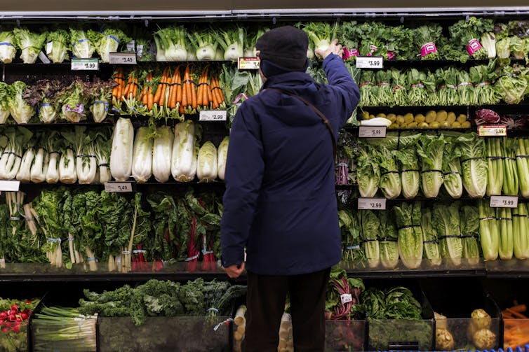 A person is photographed from behind while standing in front of a produce display.