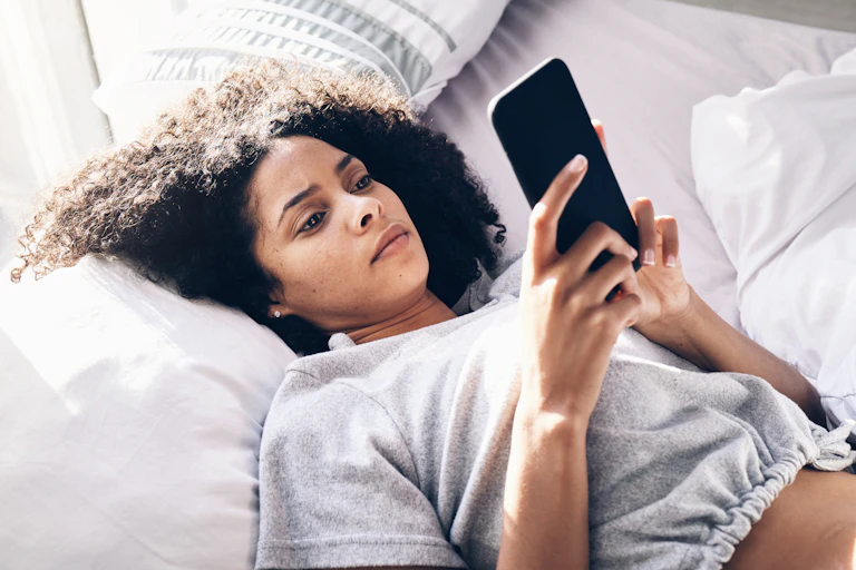 A young woman lying on a bed looking at a phone