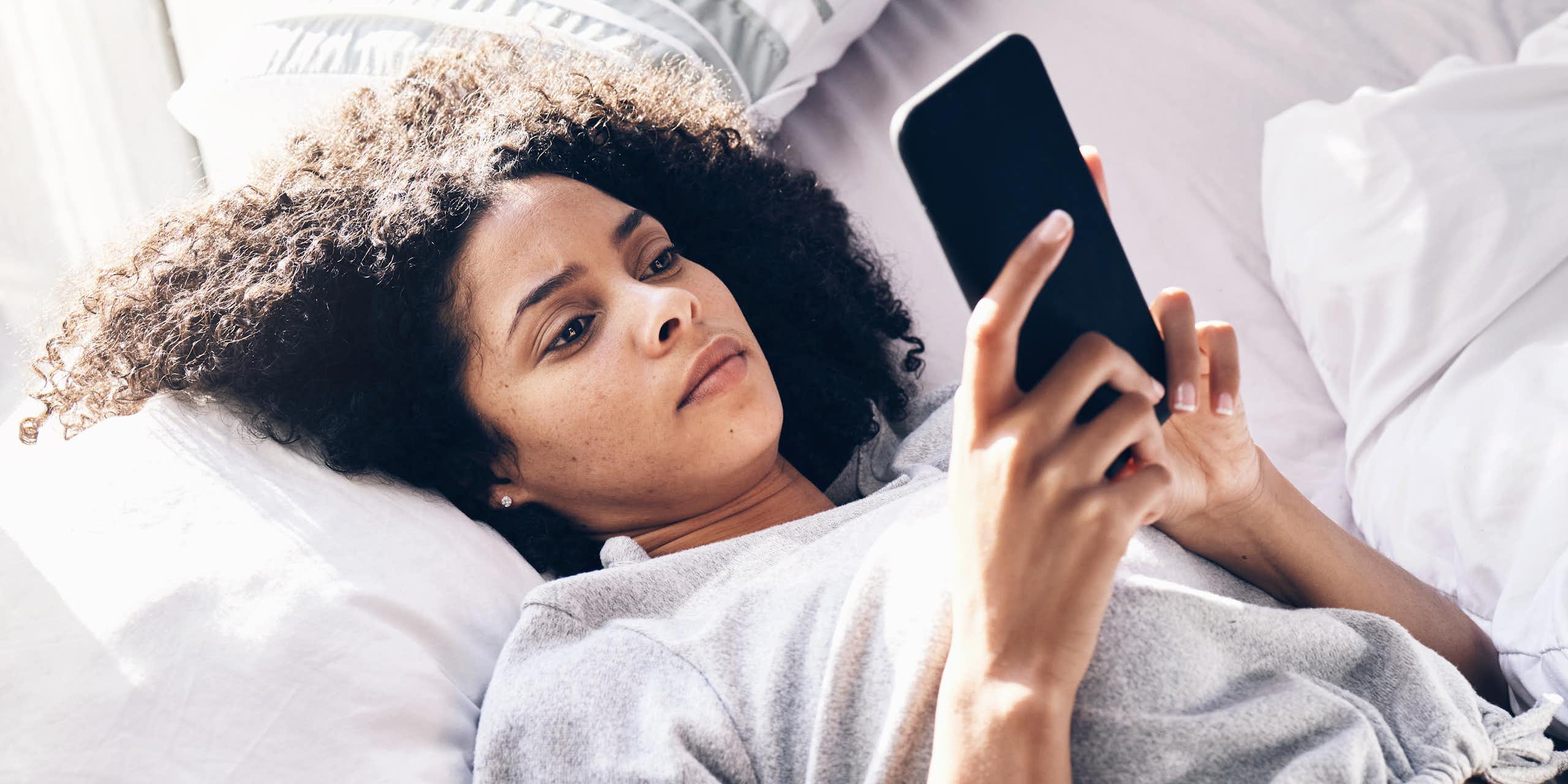 A young woman lying on a bed looking at a phone