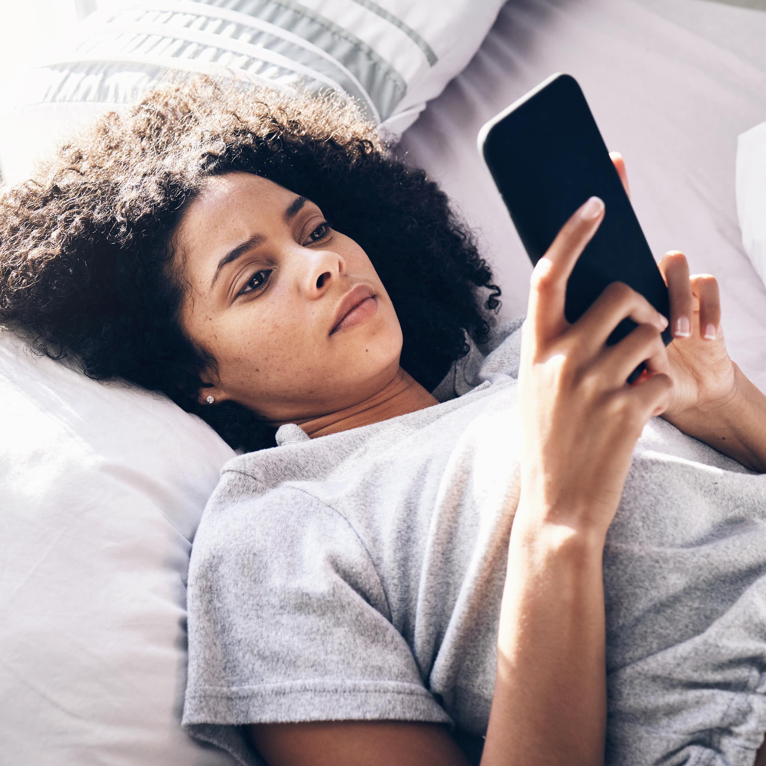 A young woman lying on a bed looking at a phone