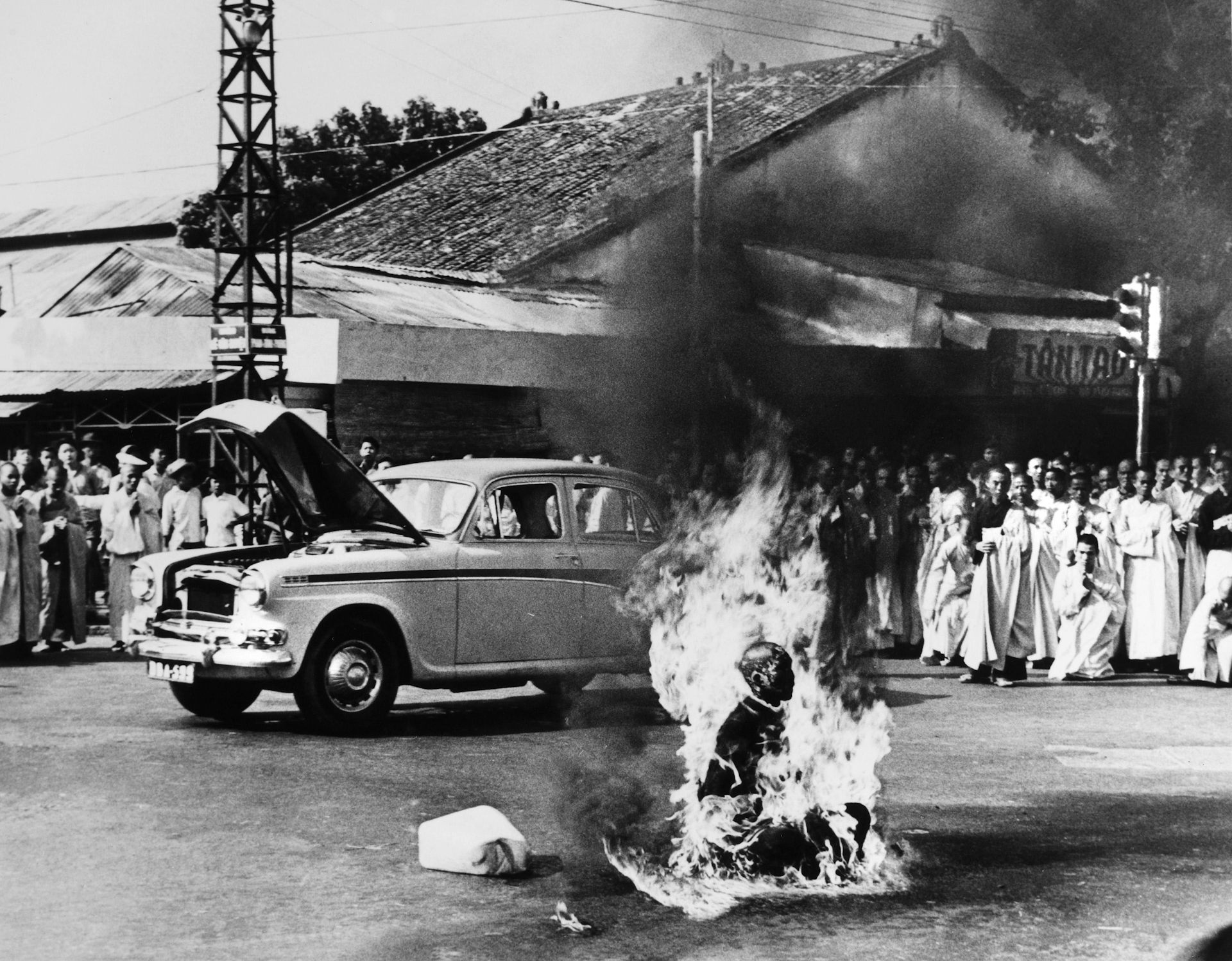 A black and white image of a Buddhist monk setting himself on fire on a road with a crowd watching on.