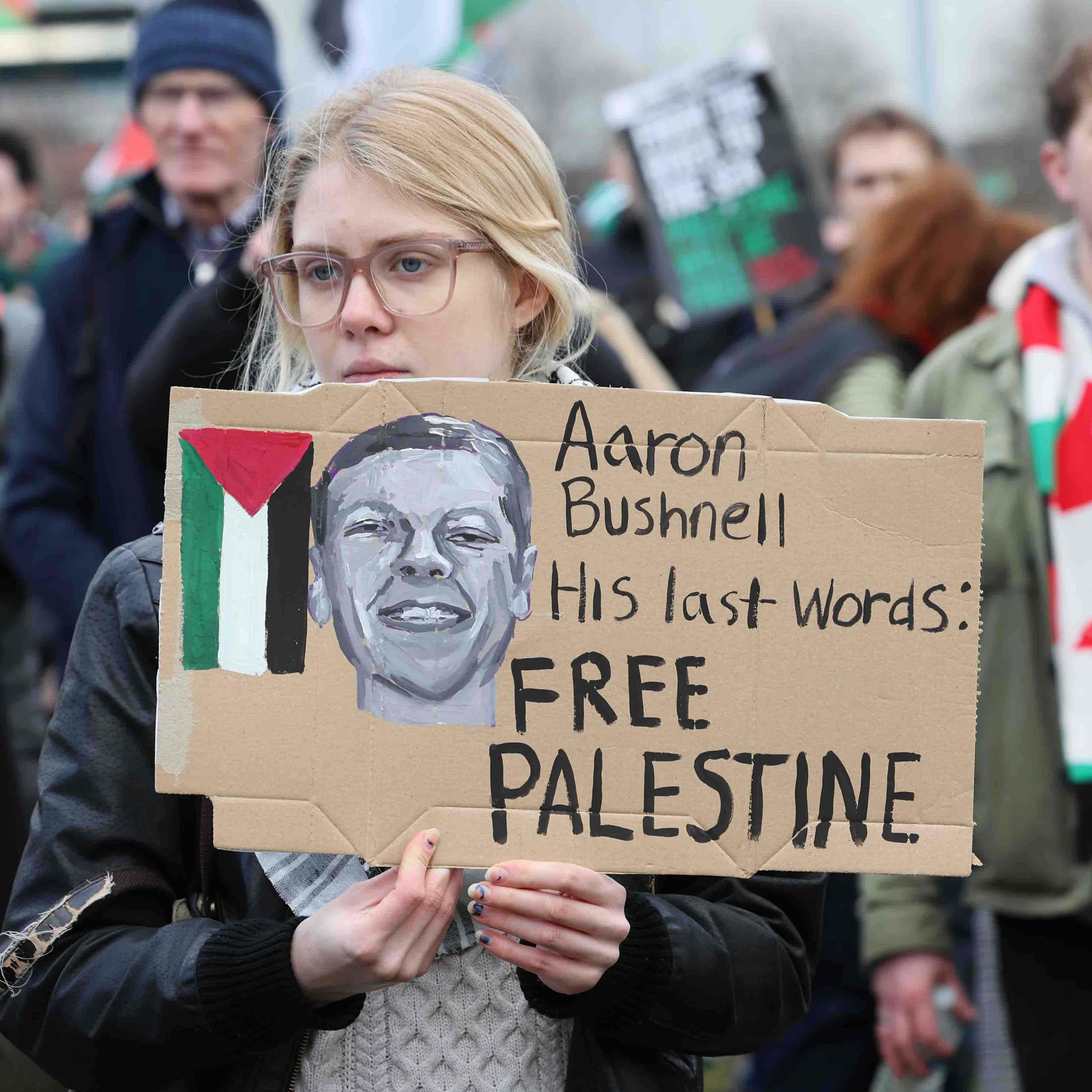 A protestor holding a placard reading "Aaron Bushnell, His last words: Free Palestine"