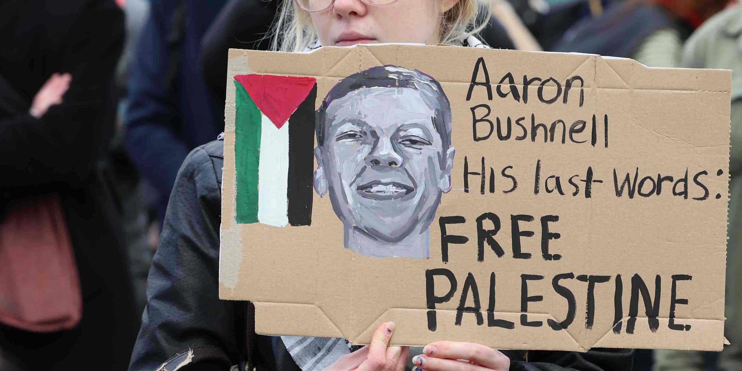 A protestor holding a placard reading "Aaron Bushnell, His last words: Free Palestine"