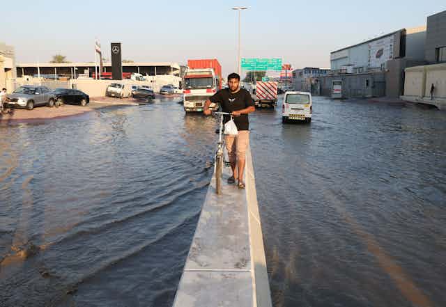 A man wheels a bicycle atop the diving barrier of a flooded motorway.