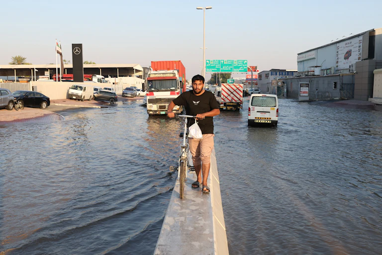 A man wheels a bicycle atop the diving barrier of a flooded motorway.