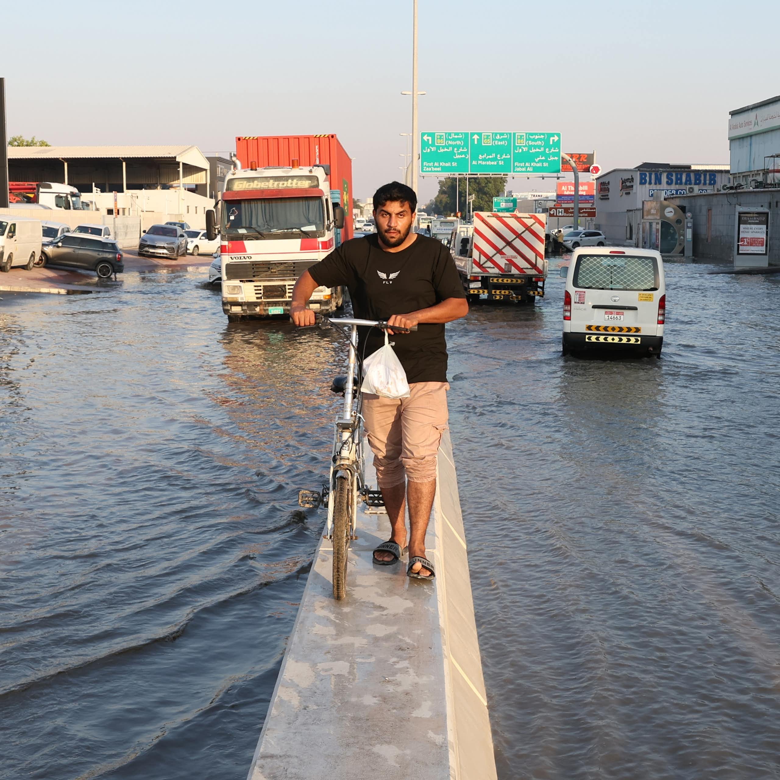 A man wheels a bicycle atop the diving barrier of a flooded motorway.