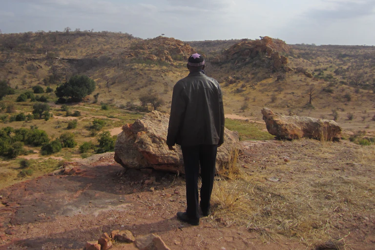 A man wearing black clothes and a yarmulke looks out across a mountainous landscape