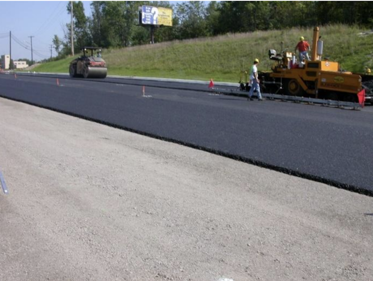 A machine drives over dark pavement.