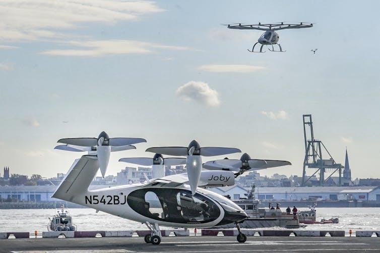 Two style of eVTOL, both with propellers that lift them vertically, with New York Harbor in the background.
