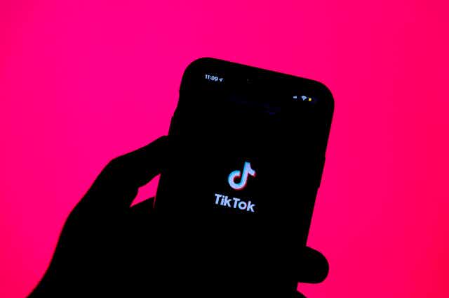 silhouette of a hand holding a smartphone with an app splash screen visible on the phone
