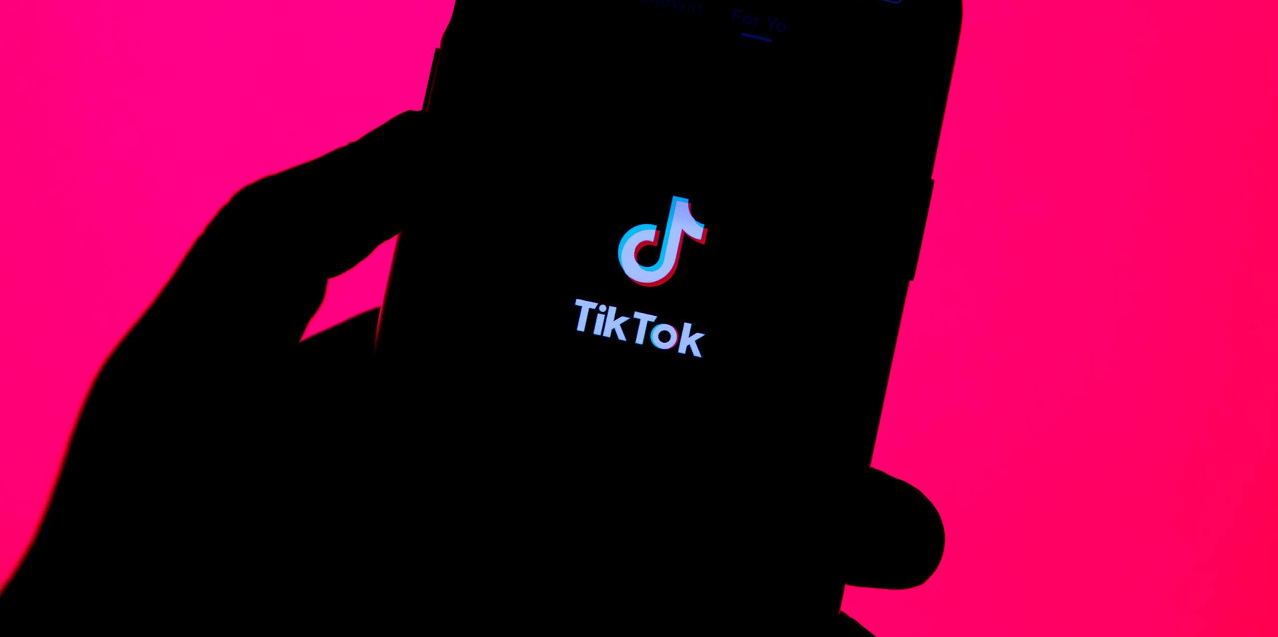 silhouette of a hand holding a smartphone with an app splash screen visible on the phone