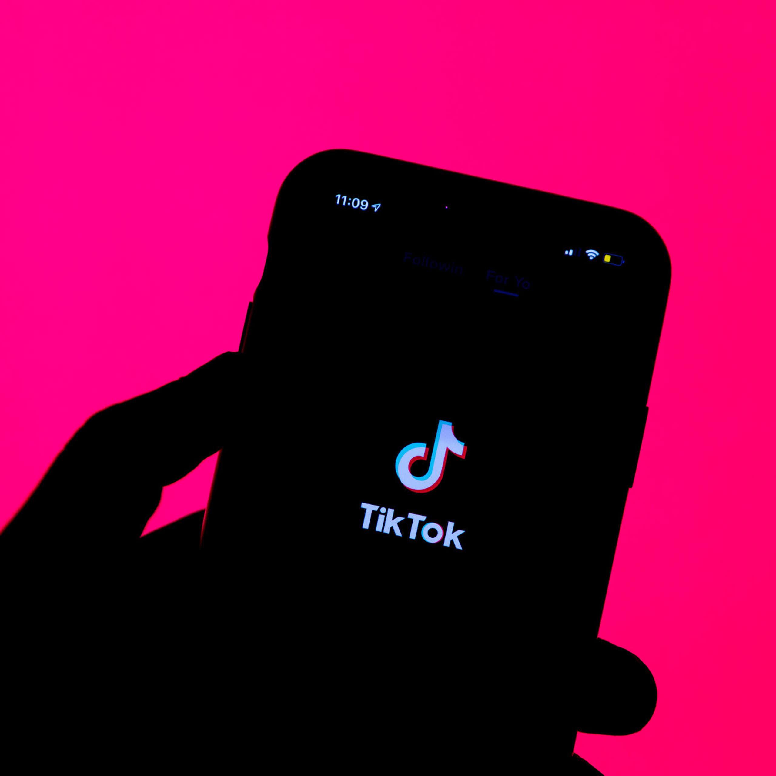 silhouette of a hand holding a smartphone with an app splash screen visible on the phone