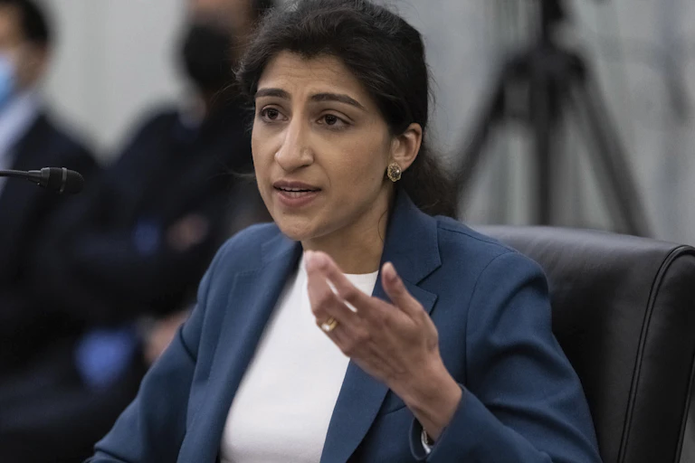 A woman in a blue blazer and white shirt speaks into a mic.