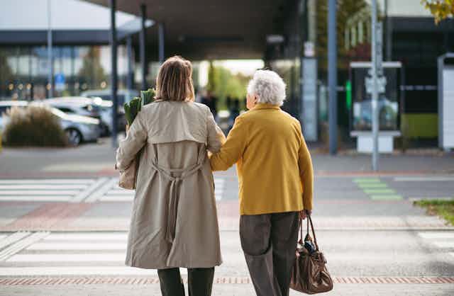 A young and older woman seen from behind walking across a street holding hands