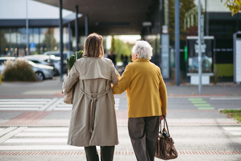 A young and older woman seen from behind walking across a street holding hands