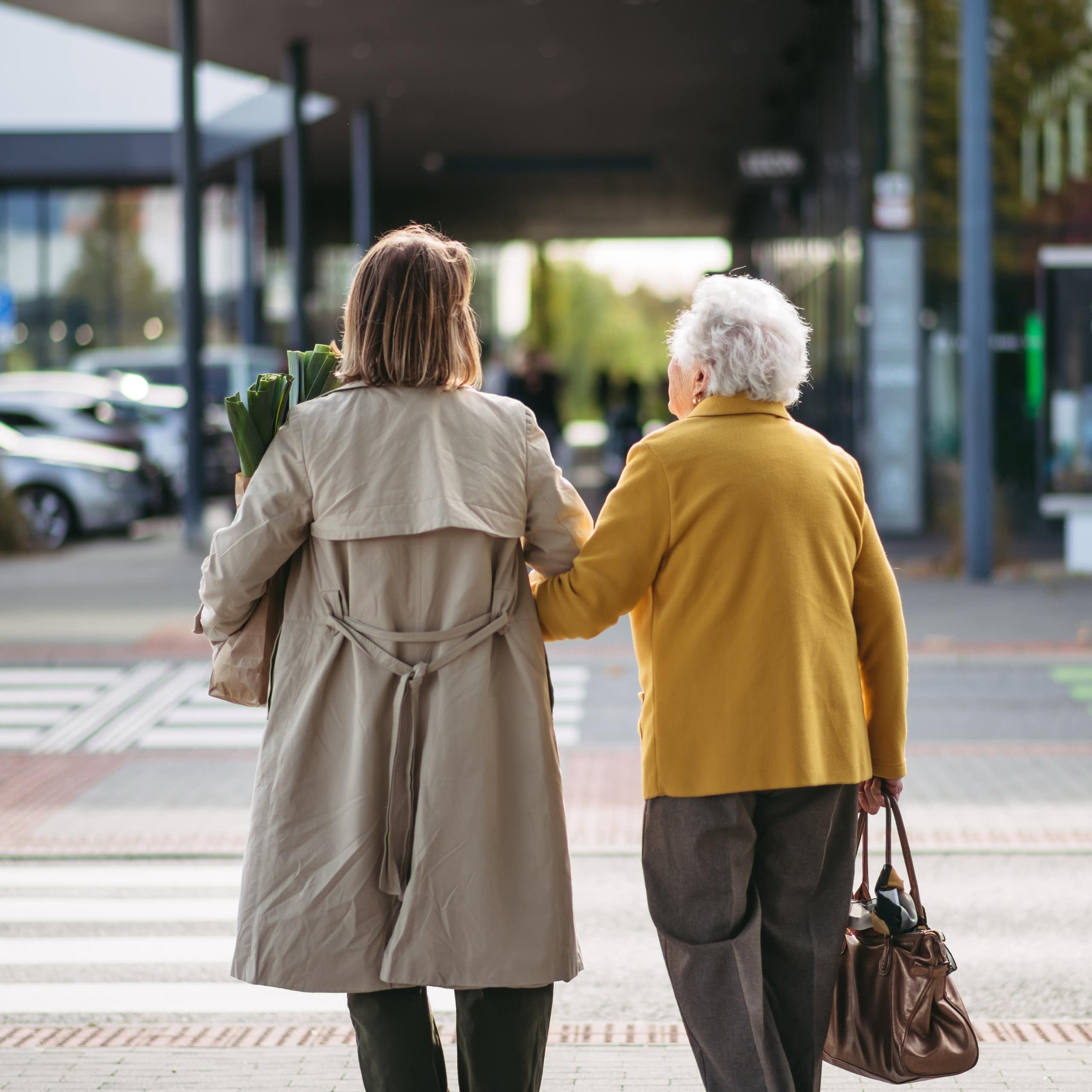 A young and older woman seen from behind walking across a street holding hands