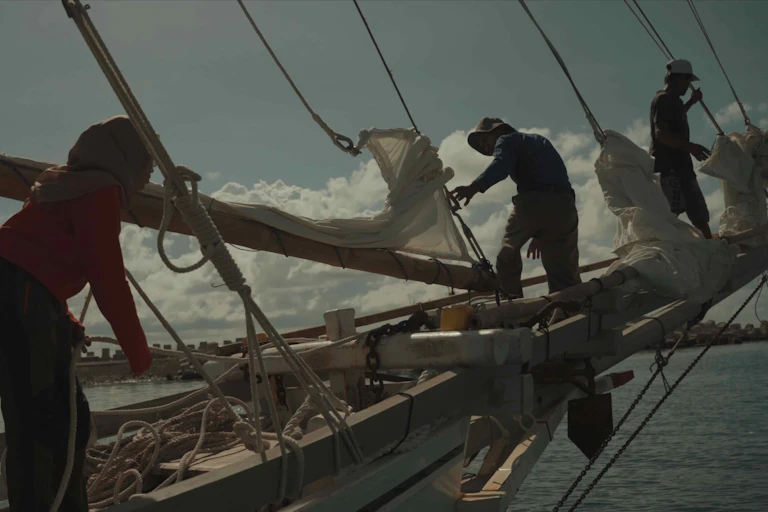 People working on the sails of a traditional boat