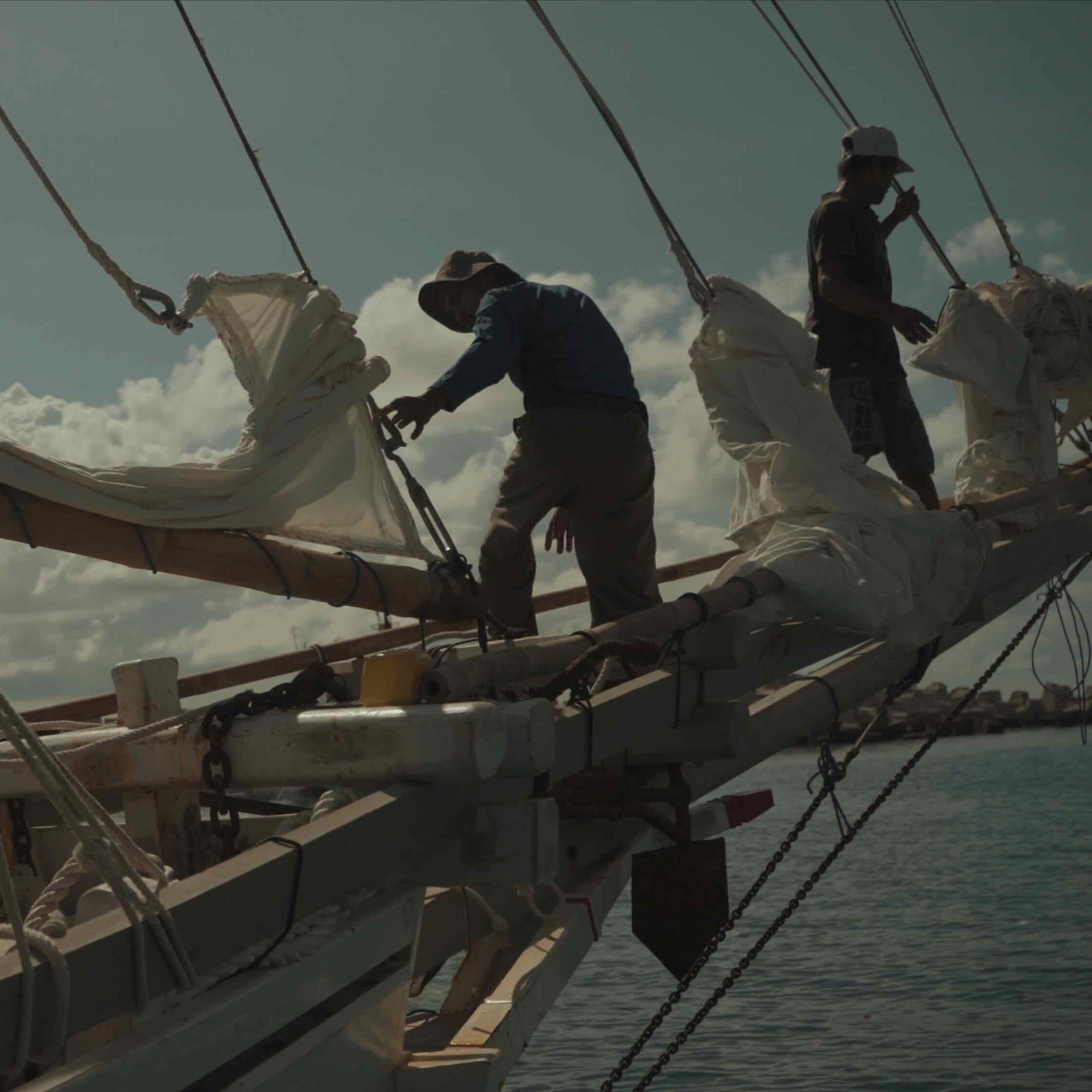 People working on the sails of a traditional boat