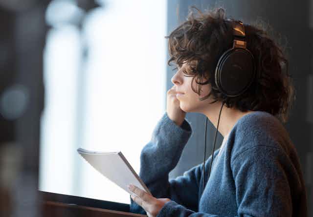 A woman listening to headphones with a neutral expression