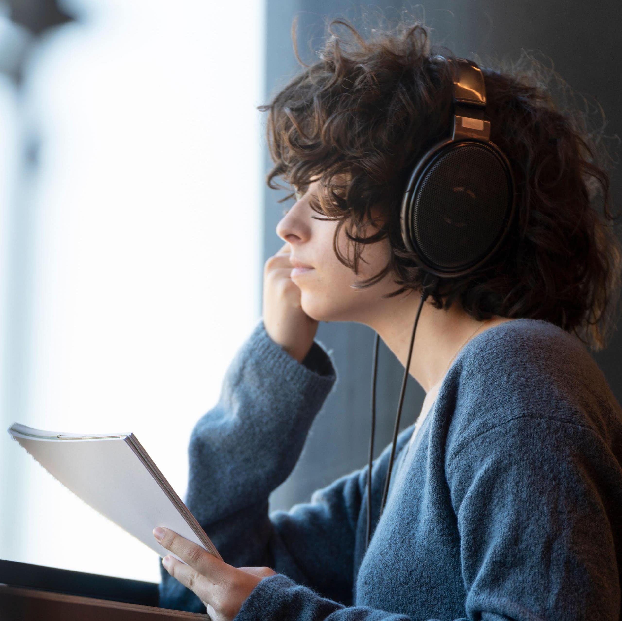 A woman listening to headphones with a neutral expression