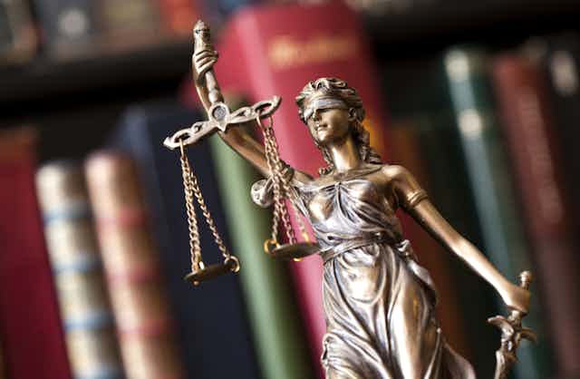 Small statue of Justice holding a set of scales, with an out of focus bookshelf in the background