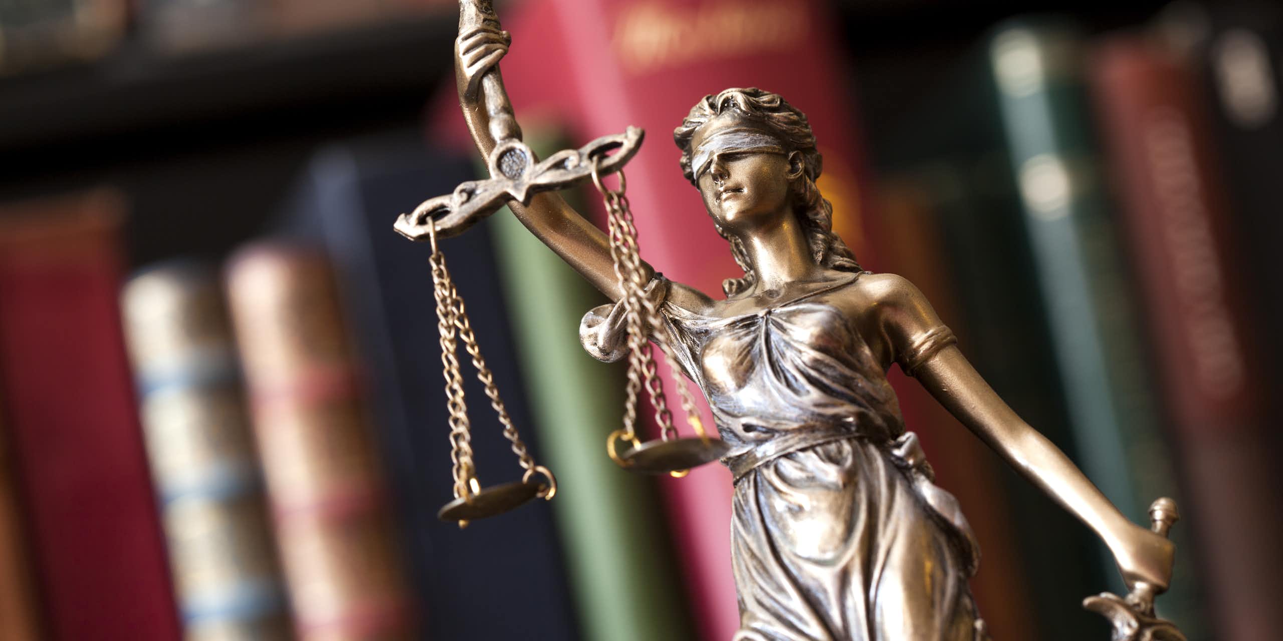 Small statue of Justice holding a set of scales, with an out of focus bookshelf in the background