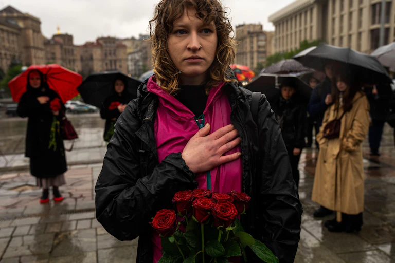 A yong woman stands in the rain at a funeral in KHarkiv, Ukraine, with her hand on her heart.
