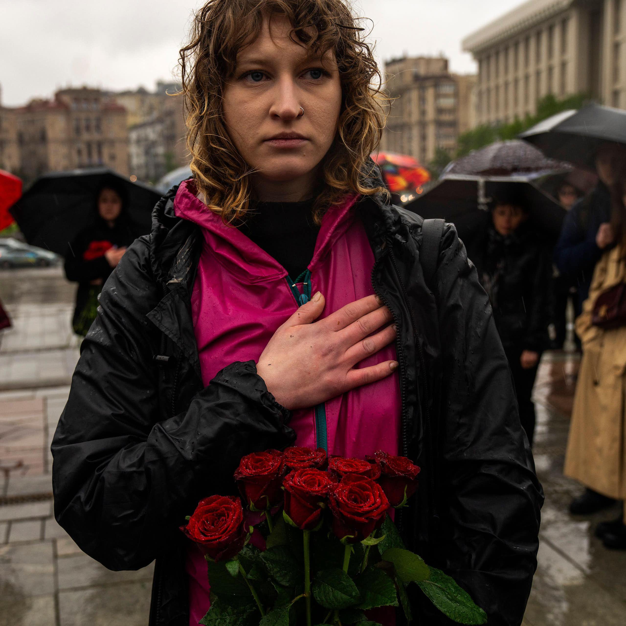 A yong woman stands in the rain at a funeral in KHarkiv, Ukraine, with her hand on her heart.
