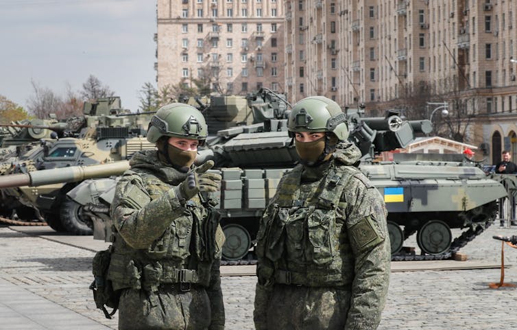 Two Ukrainian soldiers stand in front of tanks.