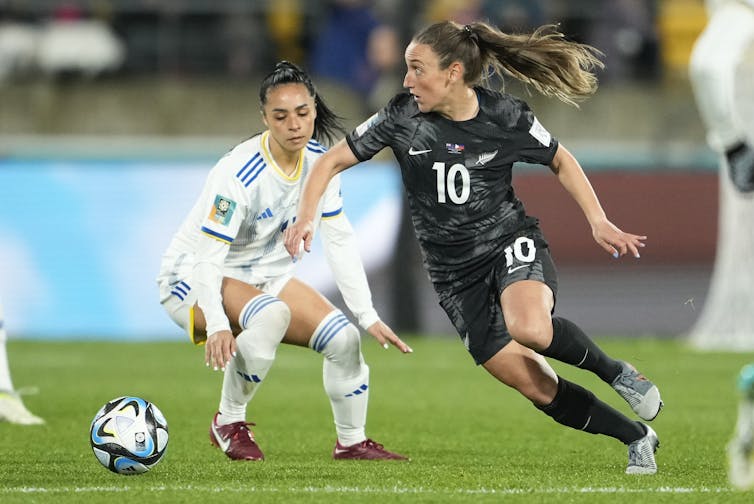 Two women play soccer, one is in motion, clearly sprinting to kick the ball.