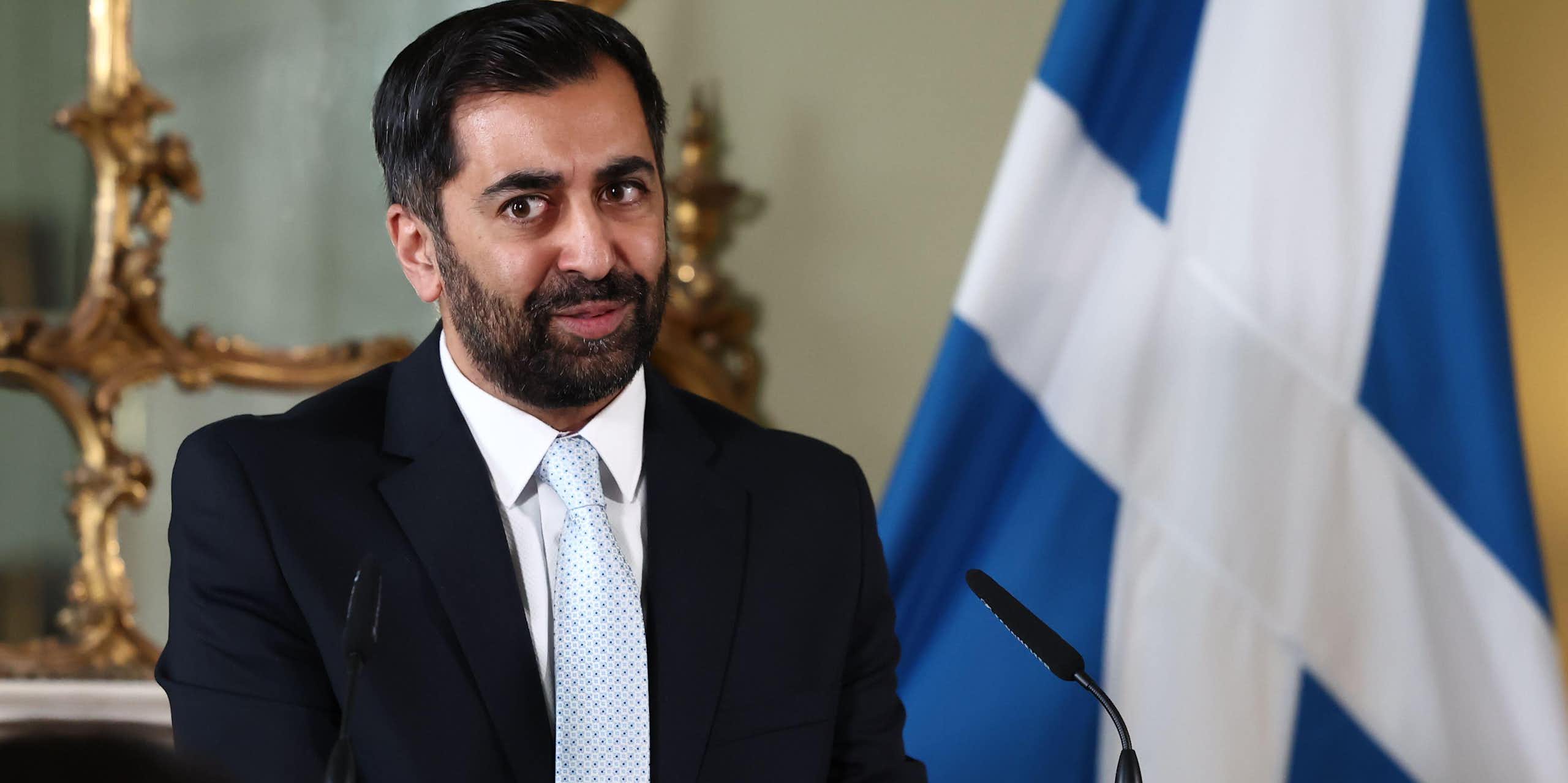 Humza Yousaf giving a speech in front of a Scottish flag. 