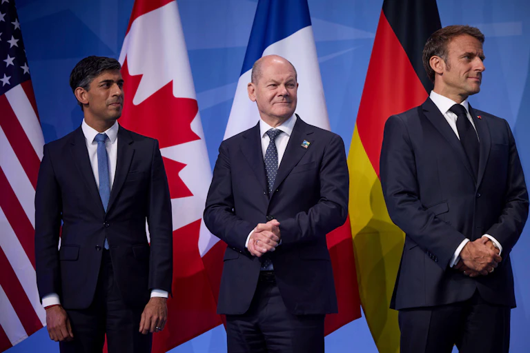 Rishi Sunak, Olaf Scholz, and Emmanuel Macron in front of flags.